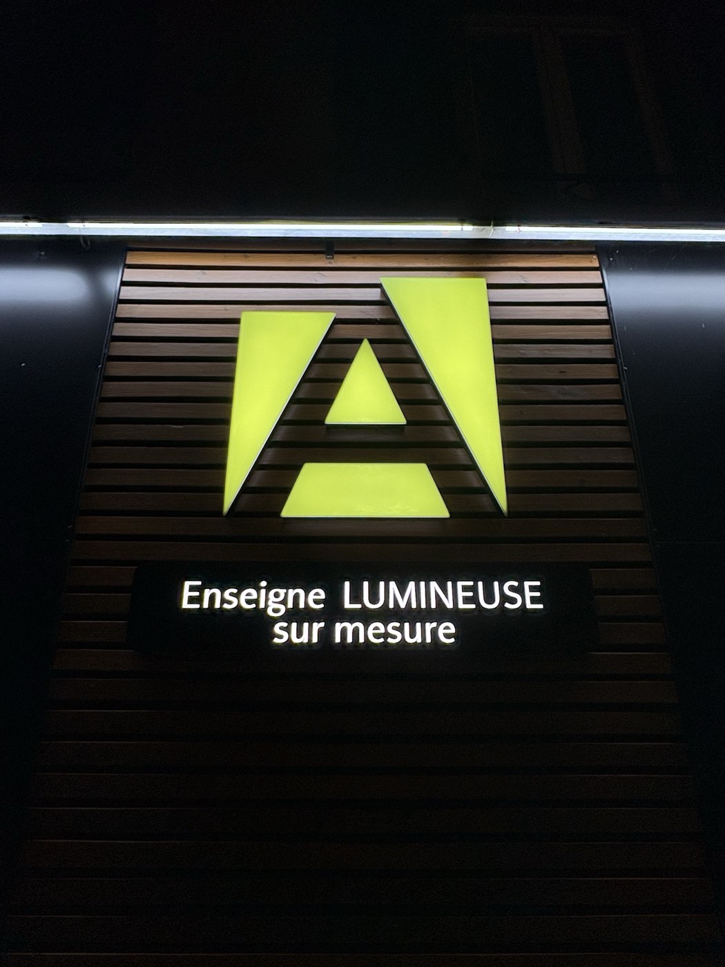 Le A lumineux de l'enseigne Aveline et sa plaque, la nuit, sur bardage bois